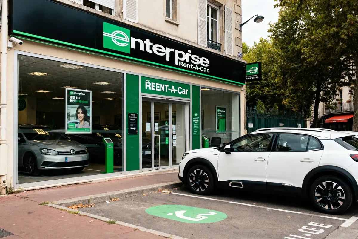 Agence de location de voitures Enterprise avec une voiture blanche garée devant l'entrée.