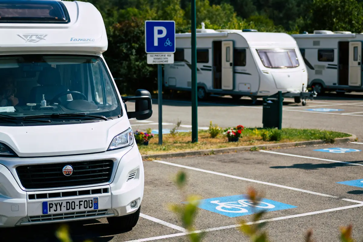 Camping-car blanc garé sur une place réservée aux personnes handicapées, panneau de signalisation visible.